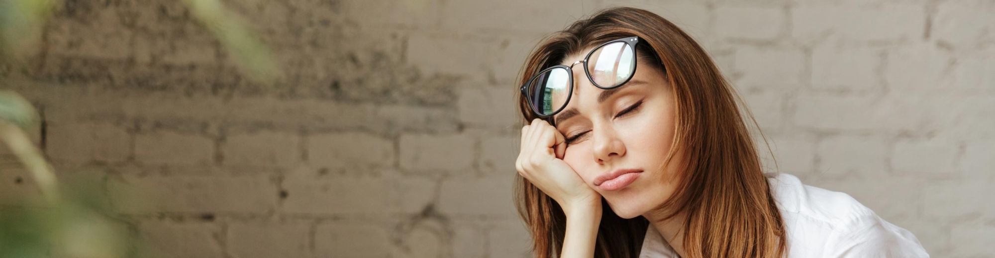Eine müde junge Frau, welche sich auf dem Tisch abstützt und die Augen schläfrig schließt.